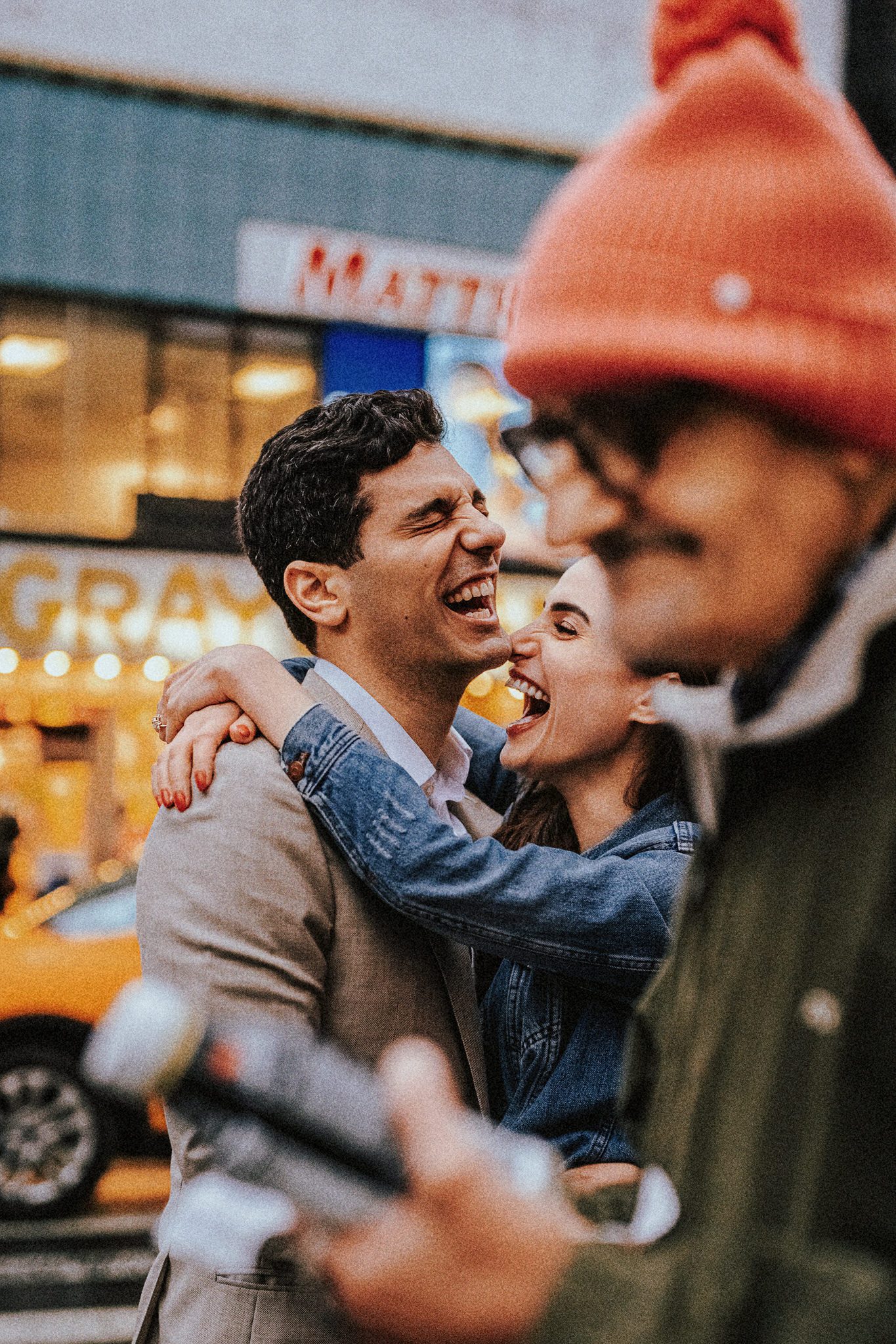 NYC engagement photo of a couple laughing together on a busy street, captured candidly in documentary style.