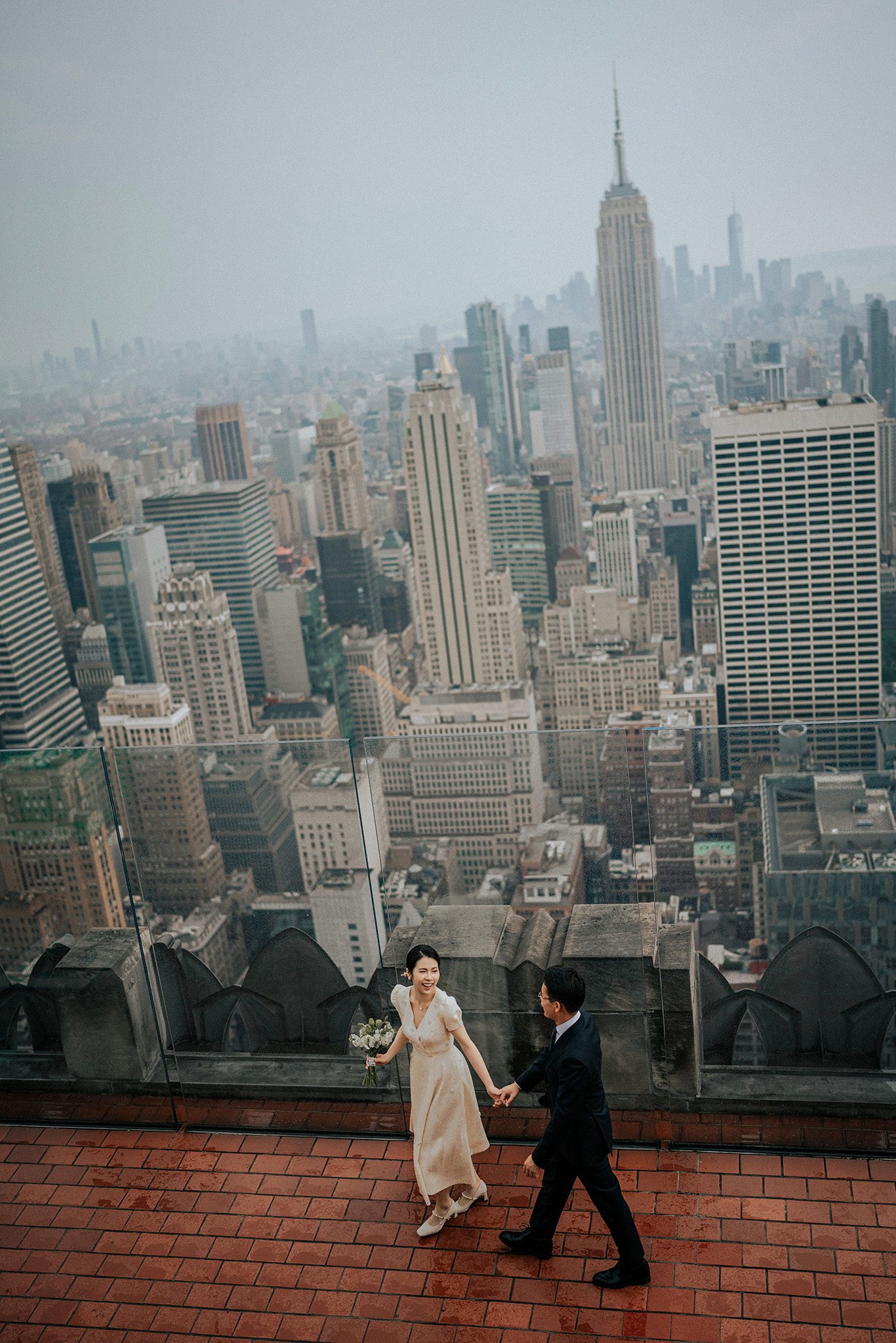 NYC pre-wedding photo at Top of the Rock with the Empire State Building in the background, captured in a candid fine-art style.