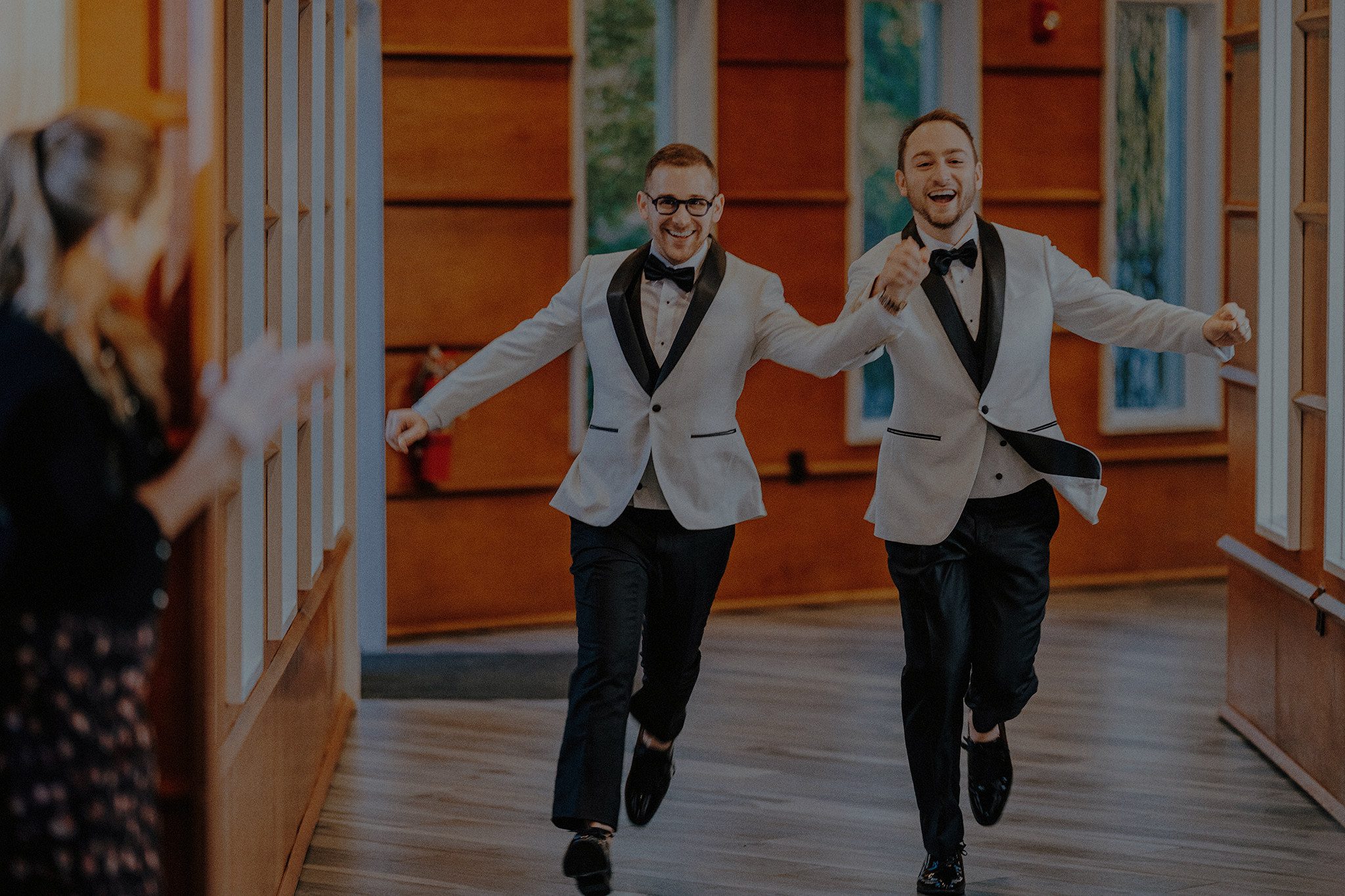 Authentic and joyful moment of two grooms running into their wedding reception, captured in a fine art documentary style that highlights genuine emotion and candid movement — Resonance Vision Photography.